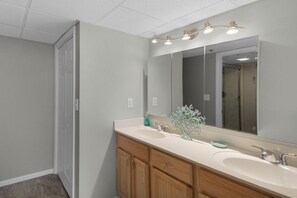 A bathroom with two sinks, wooden cabinets, a large mirror, and a ceiling light fixture. - Relax, Unwind & Soak Up the Sun – Direct Beachfront Condo, W/Beach Chair Service (Panama City Beach)
