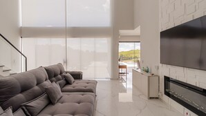 A modern living room with a large sofa, a flat-screen TV, and a view of the outdoors.
