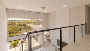 A modern interior with a balcony, a dining area, and a view of a green landscape.