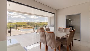 A modern dining area with a glass wall overlooking a pool and landscape.
