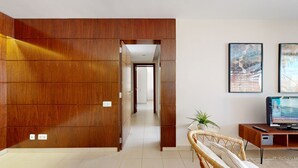 A modern living room with a wooden panel wall, a wicker chair, a television, and artwork on the wall. - Herdade dos Salgados, T2 12C_2A, Vila das Lagoas (Albufeira)