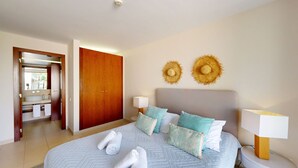 A bedroom with a bed, two bedside lamps, a headboard, and two wall-mounted hats. - Herdade dos Salgados, T2 12C_2A, Vila das Lagoas (Albufeira)