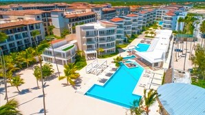 Un resort con varias edificaciones, una piscina central y palmeras.