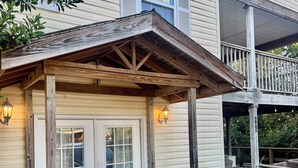 A two-story building with a covered porch, a garage door, and a 'For Sale' sign.