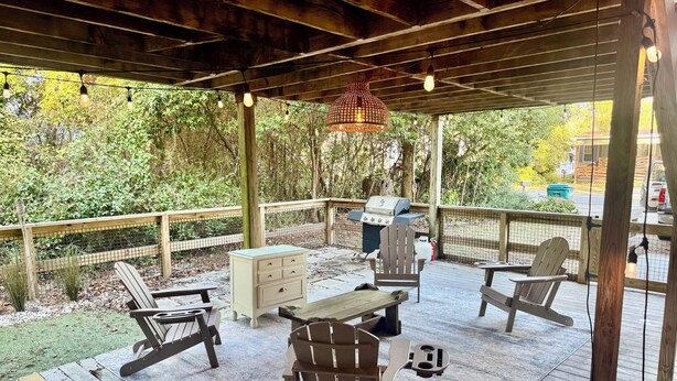 A covered outdoor deck with wooden furniture, a grill, and string lights.