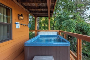 A wooden deck with a hot tub, a window, and a wooden railing. - Honey Bear Lodge, 4BR Family Cabin, Hot Tub, Views, Seasonal Resort Pool (Gatlinburg)