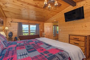 A wooden cabin bedroom with a bed, a television, and a view of the outdoors. - Honey Bear Lodge, 4BR Family Cabin, Hot Tub, Views, Seasonal Resort Pool (Gatlinburg)