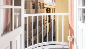 Un balcón con barandilla blanca, vistas a edificios cercanos y una puerta con ventana.