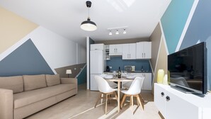 Uma sala de estar moderna com sofá, mesa de jantar, cadeiras, televisão e uma cozinha equipada com armários e eletrodomésticos.