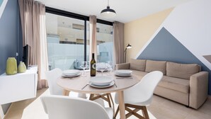 Uma sala de jantar moderna com uma mesa redonda posta para quatro pessoas, um sofá e uma janela grande com cortinas.