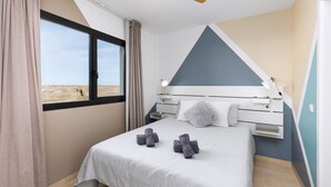Quarto com cama, ventilador de teto, janela e vista para o deserto.