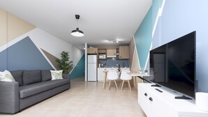 Ein modernes Wohnzimmer mit einem grauen Sofa, einem Flachbildfernseher und einem Essbereich mit einem weißen Tisch und Stühlen.
