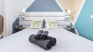 Ein ordentlich bezogenes Bett in Weiß und Grau, mit Kissen mit Schmetterlingsmuster und einem gefalteten grauen Handtuch.