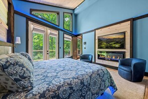 A bedroom with a large bed, a fireplace, and a view of greenery. - Nestled in the heart of Gatlinburg, "Waterfalls and Wildflowers" offers a serene (Gatlinburg)