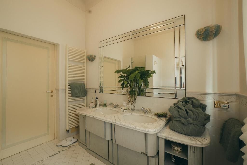 Un baño con lavamanos doble, un espejo grande, un perchero para toallas y una planta.
