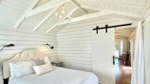 Quarto com teto inclinado, cama com cabeceira e piso de madeira.