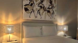Ein Schlafzimmer mit einem großen Bett, zwei Nachttischen mit Lampen und einem an der Wand hängenden Kunstwerk.