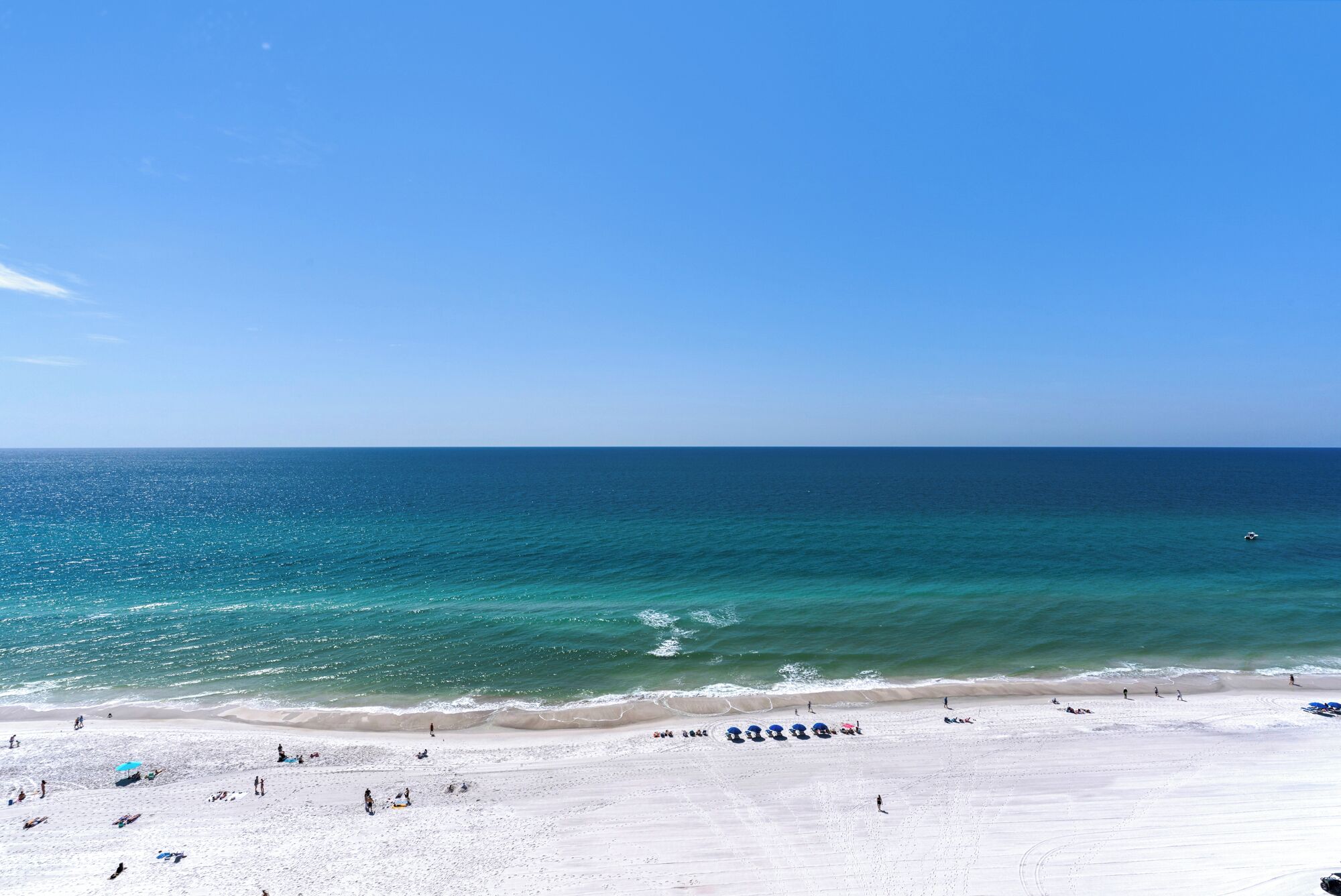A beach with clear blue water, white sand, and a few people and umbrellas.