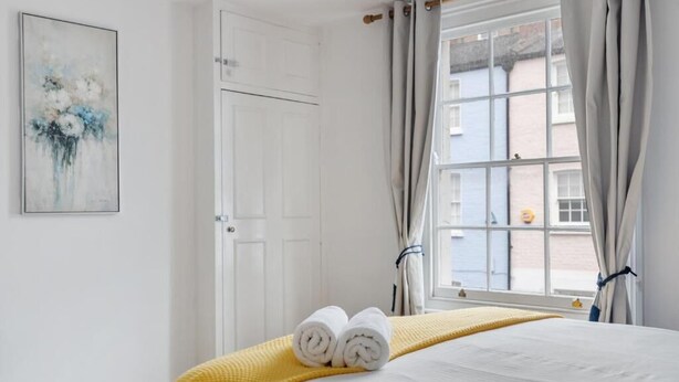 Een hotelkamer met een bed, een schilderij aan de muur en een raam met gordijnen.