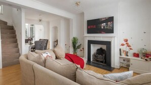 Een moderne woonkamer met een beige bank, een open haard en een Netflix-bordje.