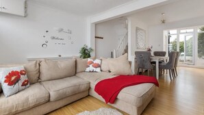 Een moderne woonkamer met een beige bank, een rode plaid en een eethoek met een tafel en stoelen.