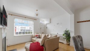 Een moderne woonkamer met een beige bank, een rode plaid, een grijze fauteuil en een groot raam met jaloezieën.