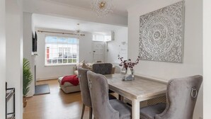 Een eetgedeelte met een houten tafel, grijs gestoffeerde stoelen, een decoratieve wandversiering en een hanglamp.