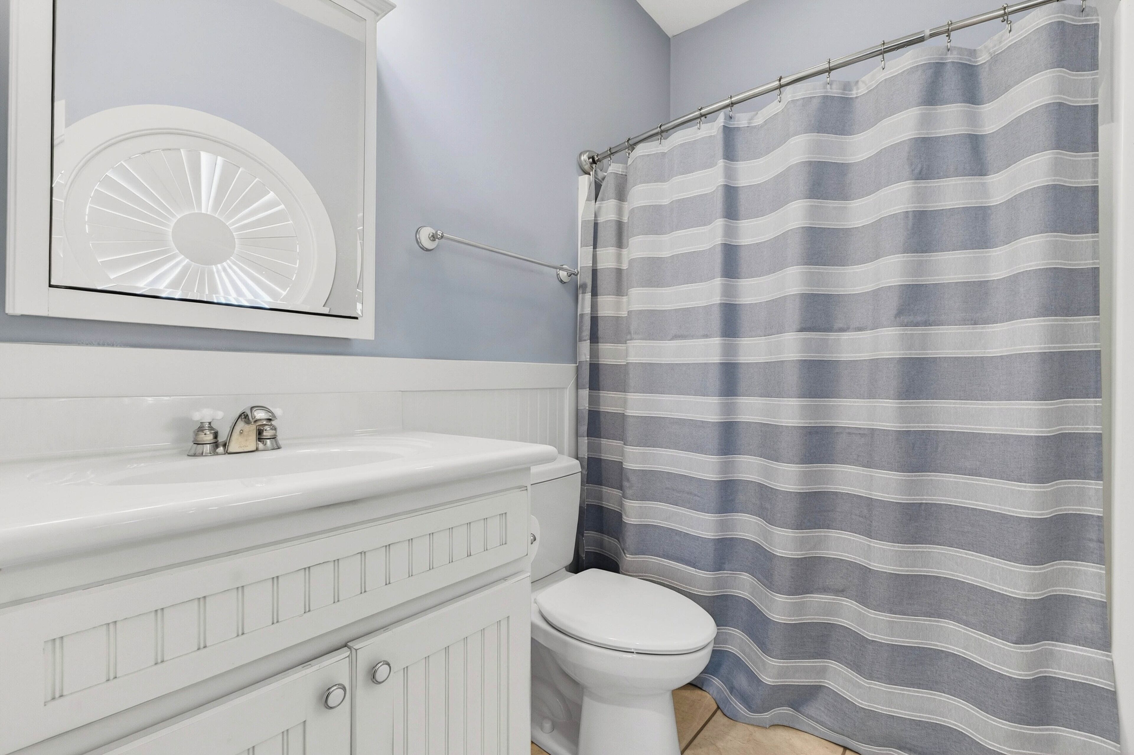 A bathroom with a white vanity, a toilet, and a shower curtain with horizontal stripes.