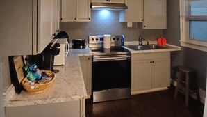 Una cocina compacta con gabinetes blancos, una estufa de acero inoxidable y un fregadero.
