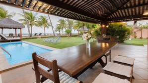 Un espace piscine extérieur doté d  ’une terrasse en bois, de chaises longues et d’une table à manger avec des coussins.