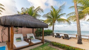 Un salon de plage doté d’un toit de chaume, de deux chaises longues, d’une petite piscine et d’une vue sur l’océan.