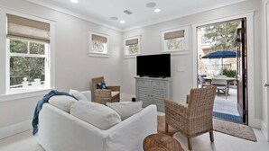 A modern living room with a white sofa, wicker chairs, a flat-screen TV, and a view of the outdoor patio. - 🏖️2BR Sea La Vie Seaside • Steps to Private Beach Access•Bikes🏖️ (Santa Rosa Beach)