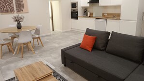 A modern living room with a grey sofa, a wooden coffee table, and a dining area with a round table and chairs.