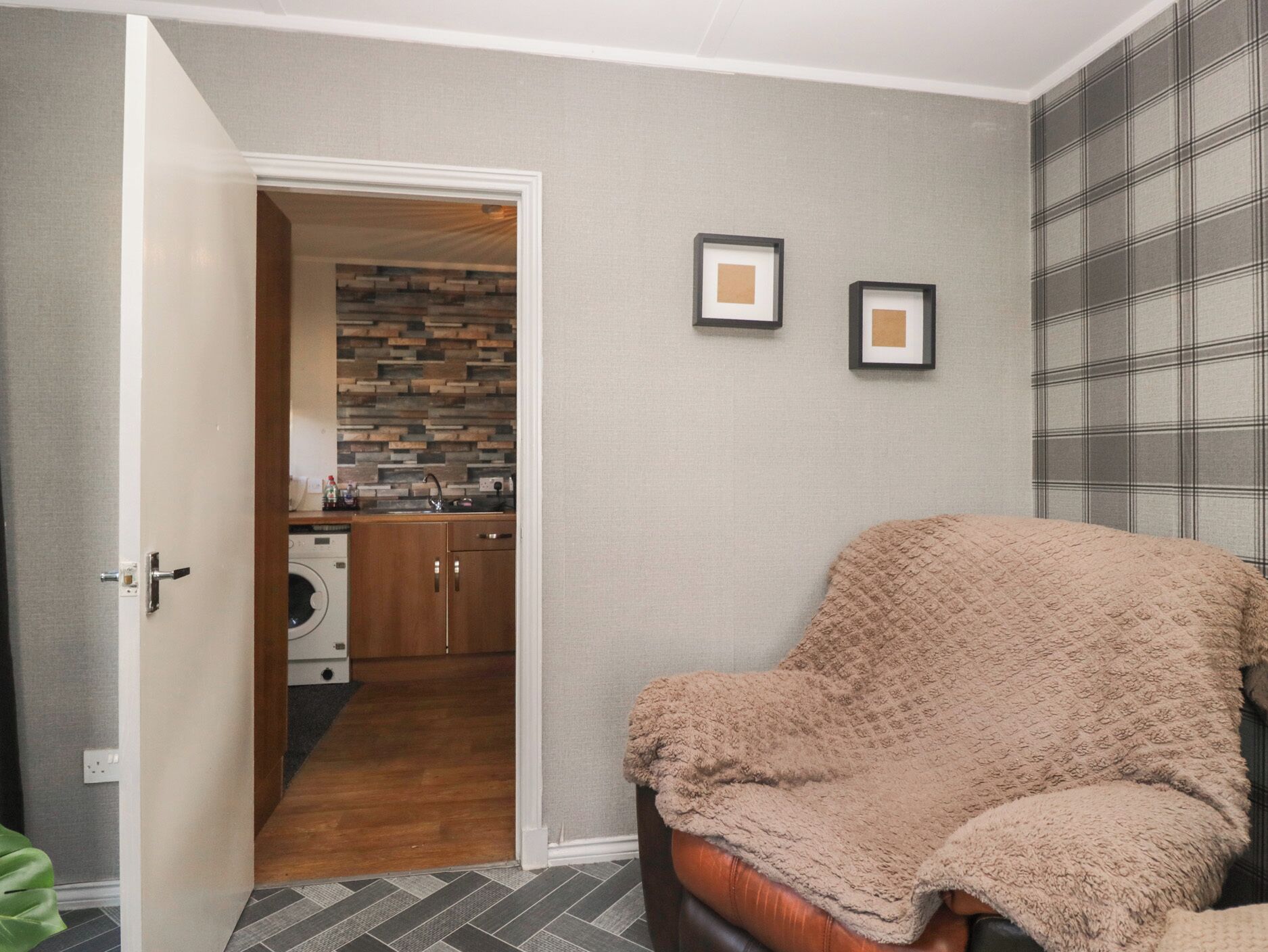 Ein Zimmer mit einer Tür zu einer Küche, einem Sofa mit Decke und zwei gerahmten Bildern an der Wand.