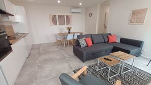 A modern living space with a grey sofa, a dining table with chairs, a kitchen area, and a patterned rug. - Bright apartment in the countryside - private parking (Fontaines-d'Ozillac)