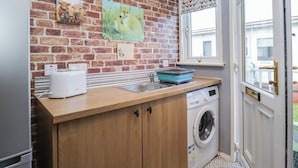 A compact kitchen with a brick wall, a washing machine, and a toaster. - Beechtree Lodge 46 (Denny)