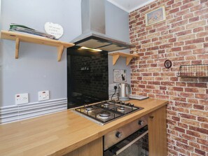 Una cucina con parete in mattoni, piano cottura a gas, bollitore e mensole in legno.