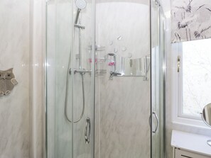 Un bagno con doccia a vetro, una parete in marmo bianco, una decorazione a forma di gufo di legno e una finestra con motivo floreale.