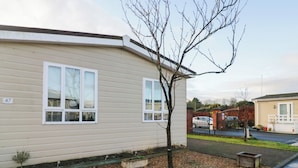 A single-story mobile home with a beige exterior, numbered 47, featuring two windows and a small tree in the front yard. - Beechtree Lodge 46 (Denny)