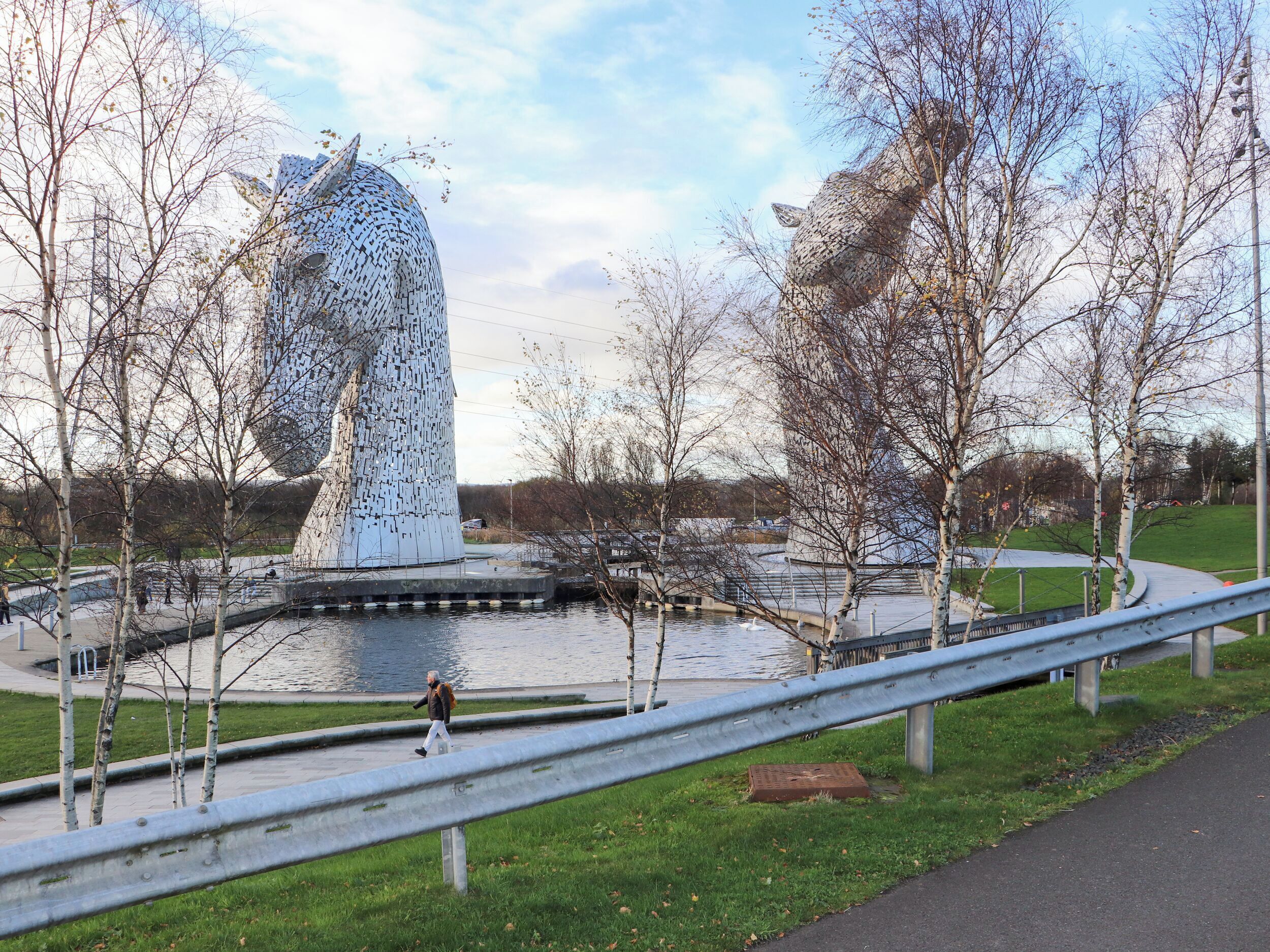 A large, metallic sculpture resembling a head with horns, surrounded by a water body and trees.