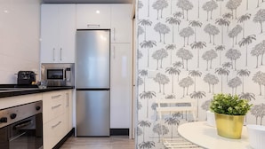 A modern kitchen with white cabinets, a stainless steel refrigerator, a microwave, and an oven. There is a white dining table with a gold pot on it. - Genteel Home Plaza del Teatro II (Malaga)