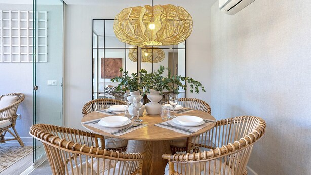 A dining area with a round wooden table, wicker chairs, and a decorative hanging light fixture. - Genteel Home Plaza del Teatro II (Malaga)