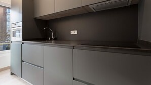 A modern kitchen with grey cabinetry, a stainless steel sink, and a built-in range hood. - Genteel Home Concha Espina I (Madrid)