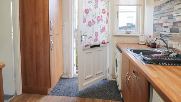 A compact kitchen with wooden cabinets, a washing machine, a sink, and a window with a view. - Beechtree Lodge 56 (Denny)