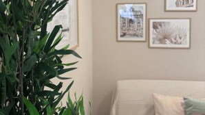 Een woonkamer met een beige bank, een grote groene plant en vier ingelijste foto's aan de muur.
