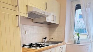 Een kleine keuken met witte kastjes, een gasfornuis, een spoelbak en een raam met gordijnen.