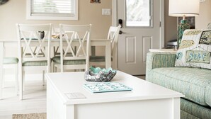 A room with a white table, two white chairs, a green sofa with 'SURF' pillows, and a decorative bowl. - Lou's Starfish Haven - Beach Front (Indian Rocks Beach)