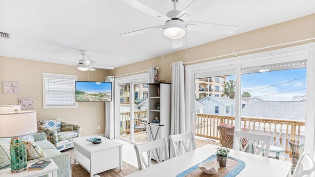 A spacious living room with a large TV, a dining table, and a balcony with a view of the neighborhood. - Lou's Starfish Haven - Beach Front (Indian Rocks Beach)