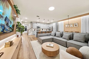 A modern living room with a sectional sofa, a wooden coffee table, and a TV mounted on the wall. - 5BR house with spa near Disney area (Kissimmee)