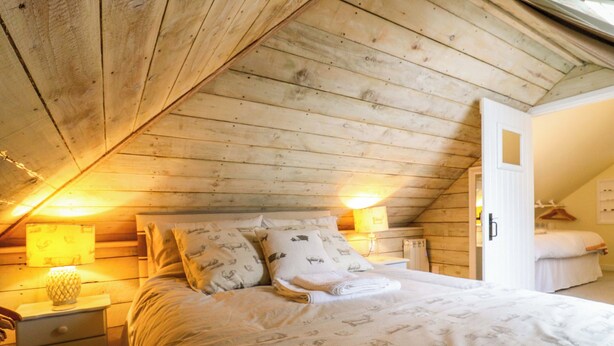 A cozy attic bedroom with a sloped ceiling, a bed with patterned bedding, a nightstand, and a dresser. - The Hayloft - Beautiful Barn Stay (Ashford)